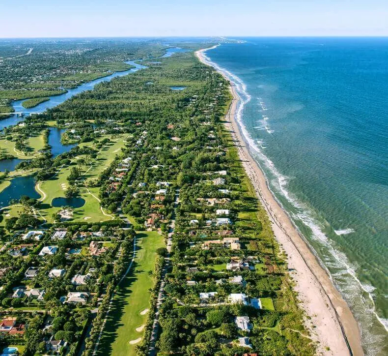 Aerial view of homes, lush green golf course, and river bordering a sandy beach on the Atlantic coastline.