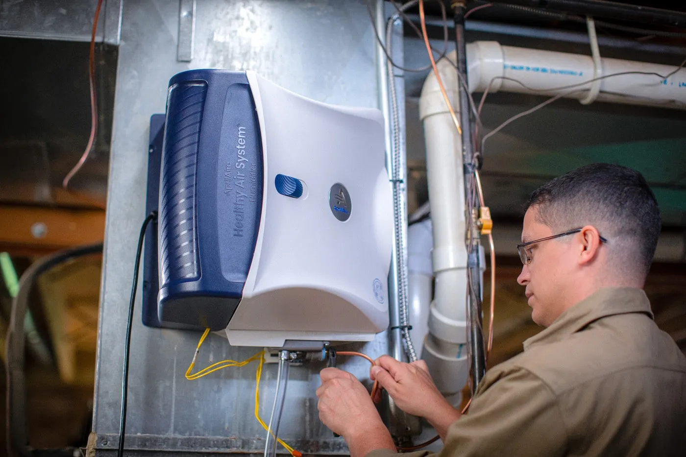 A technician installs an AprilAire Healthy Air System humidifier onto a home furnace unit.