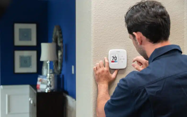 A man interacting with a white AprilAire smart thermostat mounted on a wall to control indoor temperature and humidity.